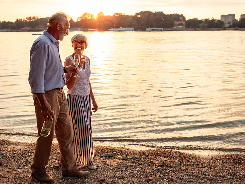 happy senior couple walking beach at sunset with glasses of wine keys to a successful retirement wilmington nc